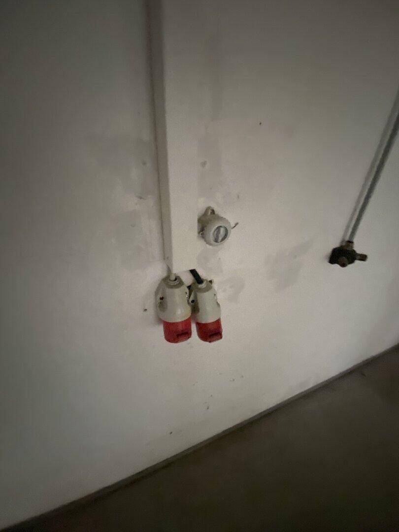 Industrielle Steckdosen und Kabel an einer Wand, weisen auf die Stromversorgung hin.