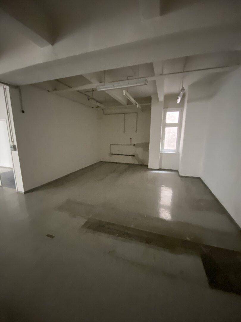 Leerer Raum mit Betonboden und sichtbaren Rohren an der Wand, geeignet als Lager oder Werkstatt.