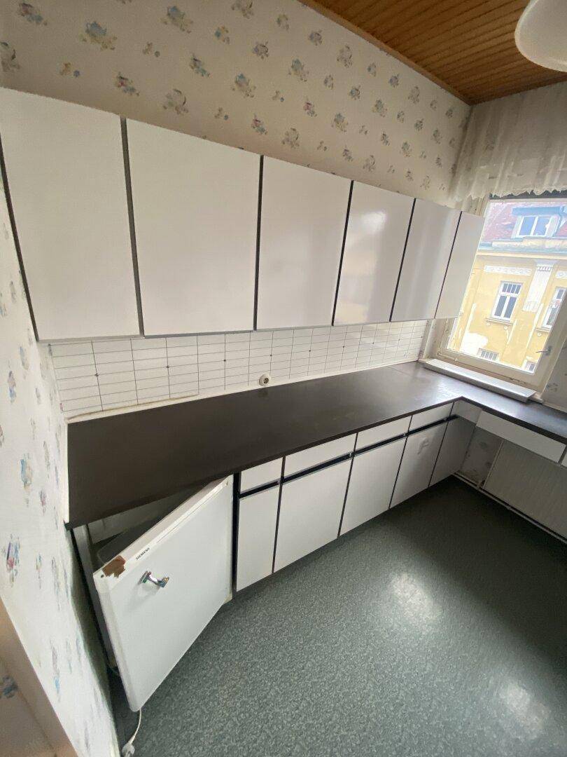 Küche mit weißen Schränken, dunkler Arbeitsplatte und einem geöffneten Unterschrank.