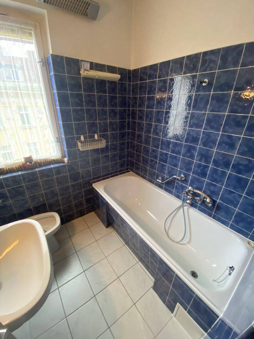 Badezimmer mit blauen Wandfliesen, Badewanne, Waschbecken und Fenster.