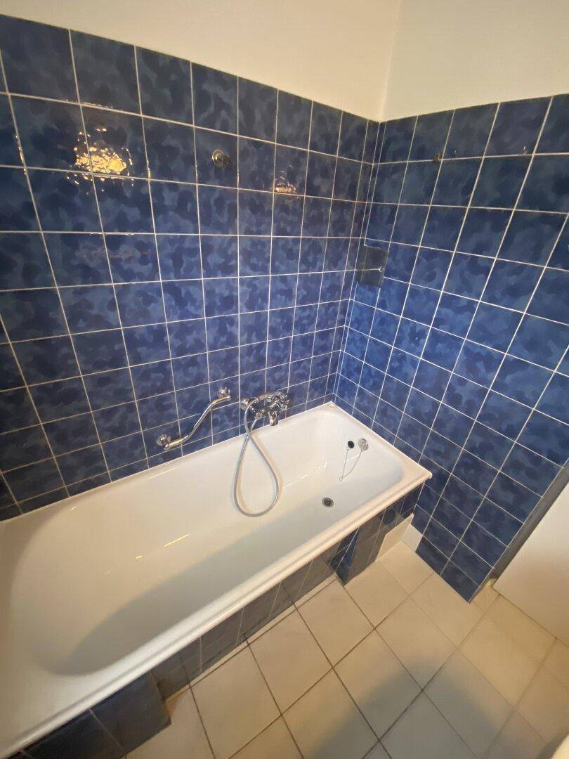 Badezimmer mit blauen Fliesen und Badewanne, die auf eine Renovierung wartet.