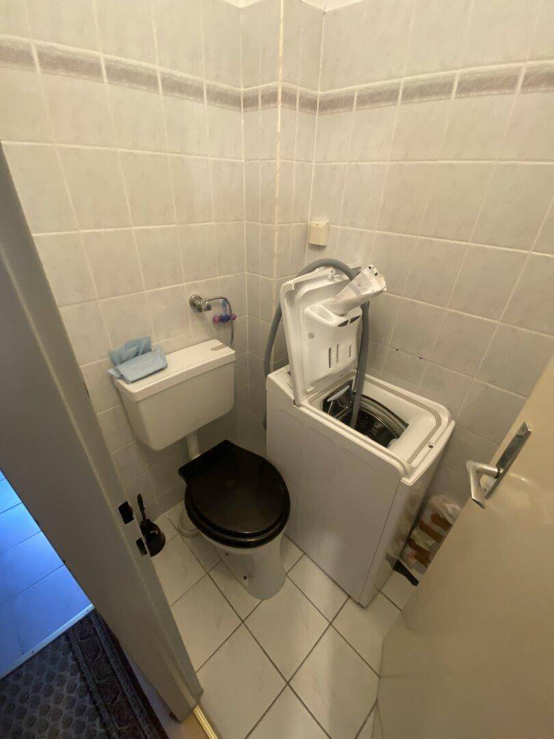 Kleiner Raum mit Toilette, Waschmaschine und hellen Wandfliesen.