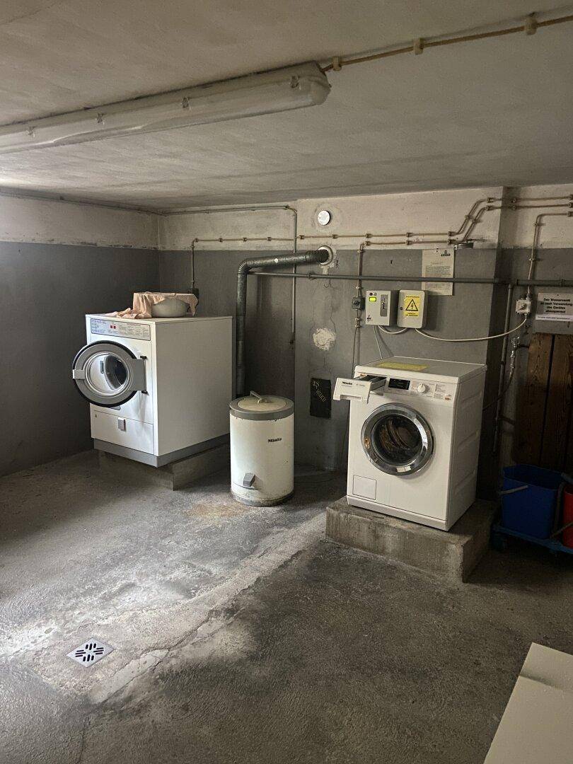 Funktionaler Gemeinschaftswaschraum im Keller mit zwei Waschmaschinen und Betonboden.
