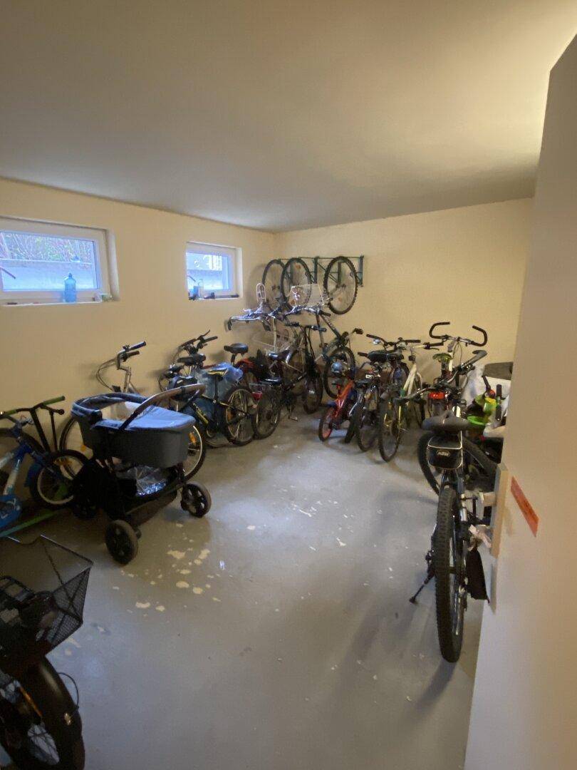 Geräumiger Fahrradabstellraum im Kellerbereich mit mehreren Fahrrädern, Kinderwagen und Fenstern.