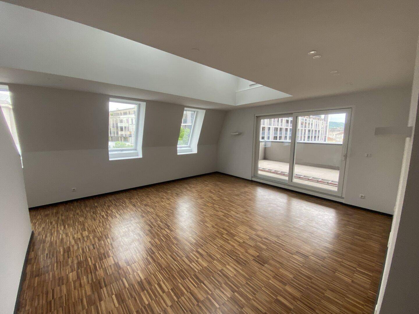 Heller Wohnraum mit Parkettboden, großen Fenstern, Dachfenster und Zugang zum Balkon.