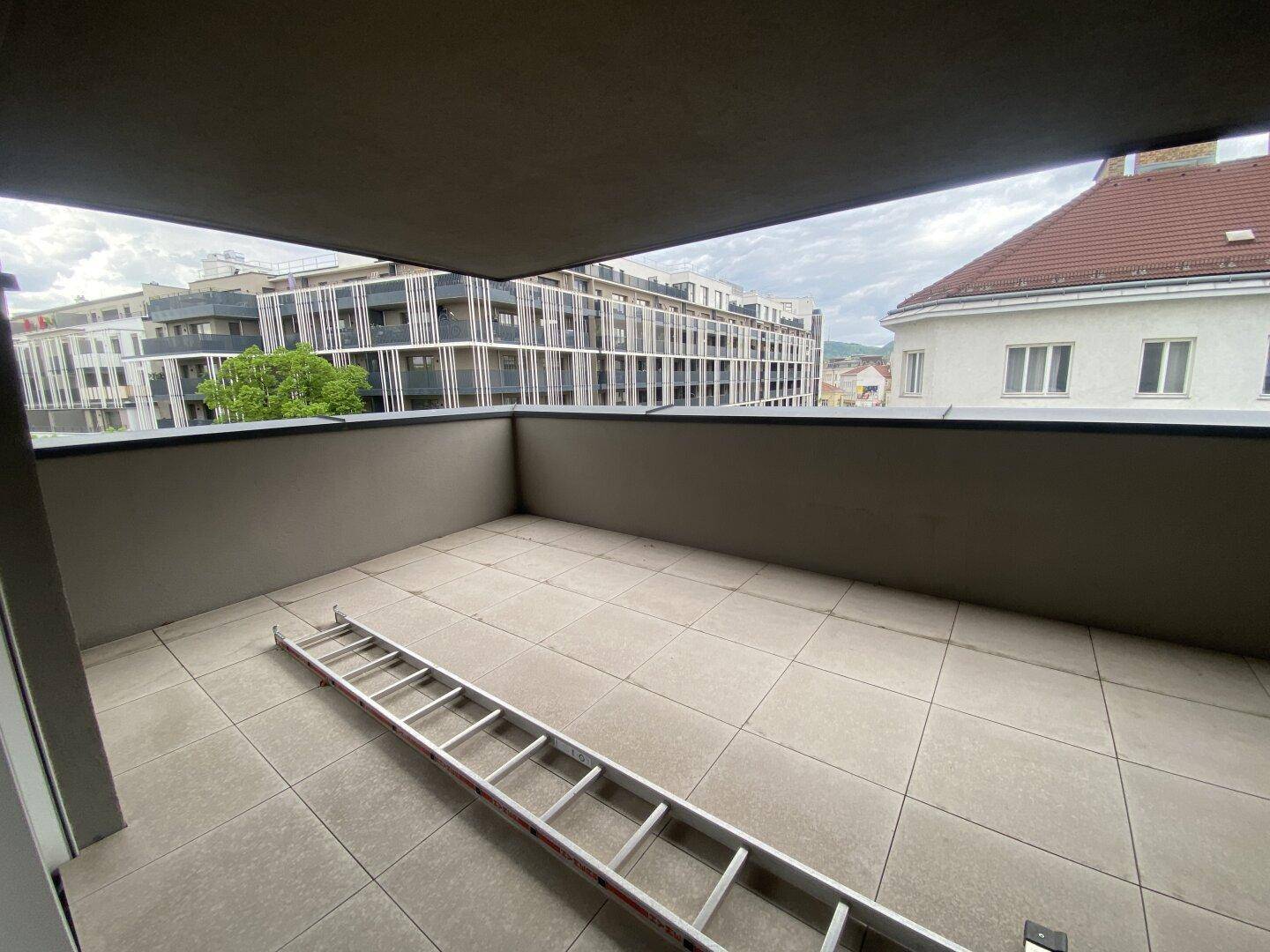 Geräumiger Balkon mit Fliesenboden und Blick auf die umliegende Stadtbebauung.