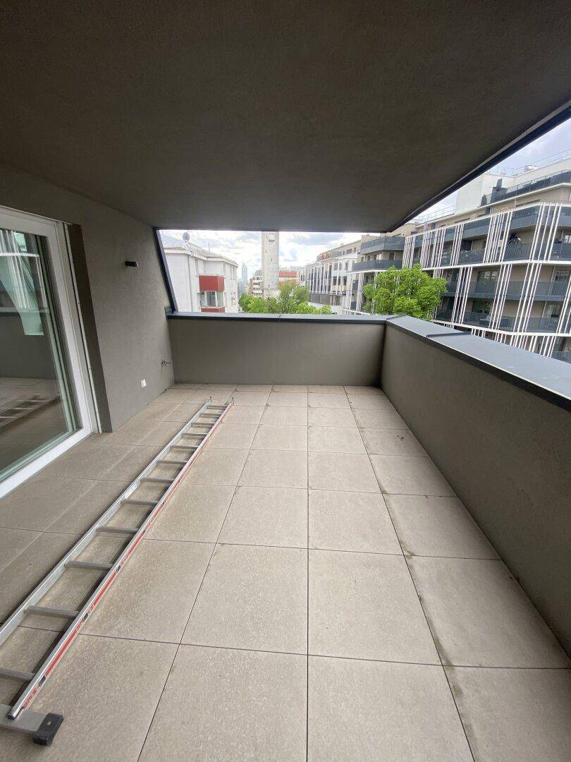 Langer Balkon mit grauen Fliesen und urbanem Ausblick auf die Nachbarschaft.