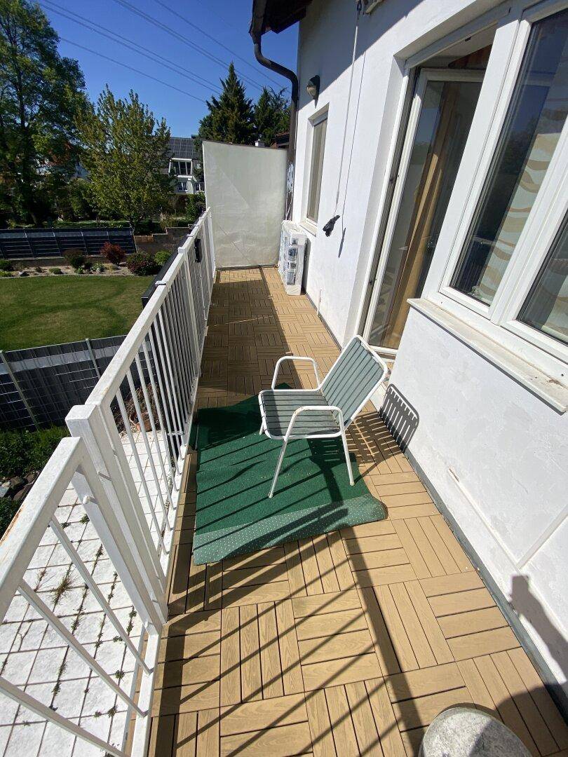 Kleiner Balkon mit Holzbodenfliesen und Blick auf den Garten.