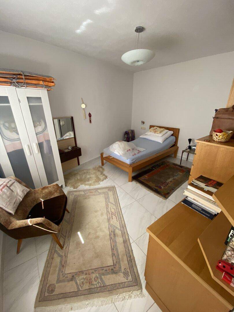 Helles Schlafzimmer mit Fliesenboden, Einzelbett und Kleiderschrank.