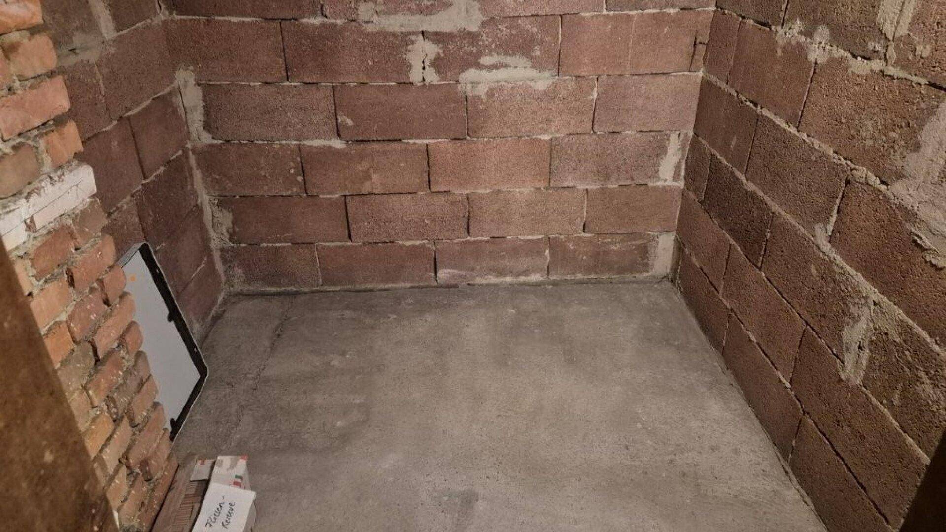 Detailansicht eines einfachen Kellerraums mit rohen Ziegelwänden und Betonboden für Lagerzwecke.
