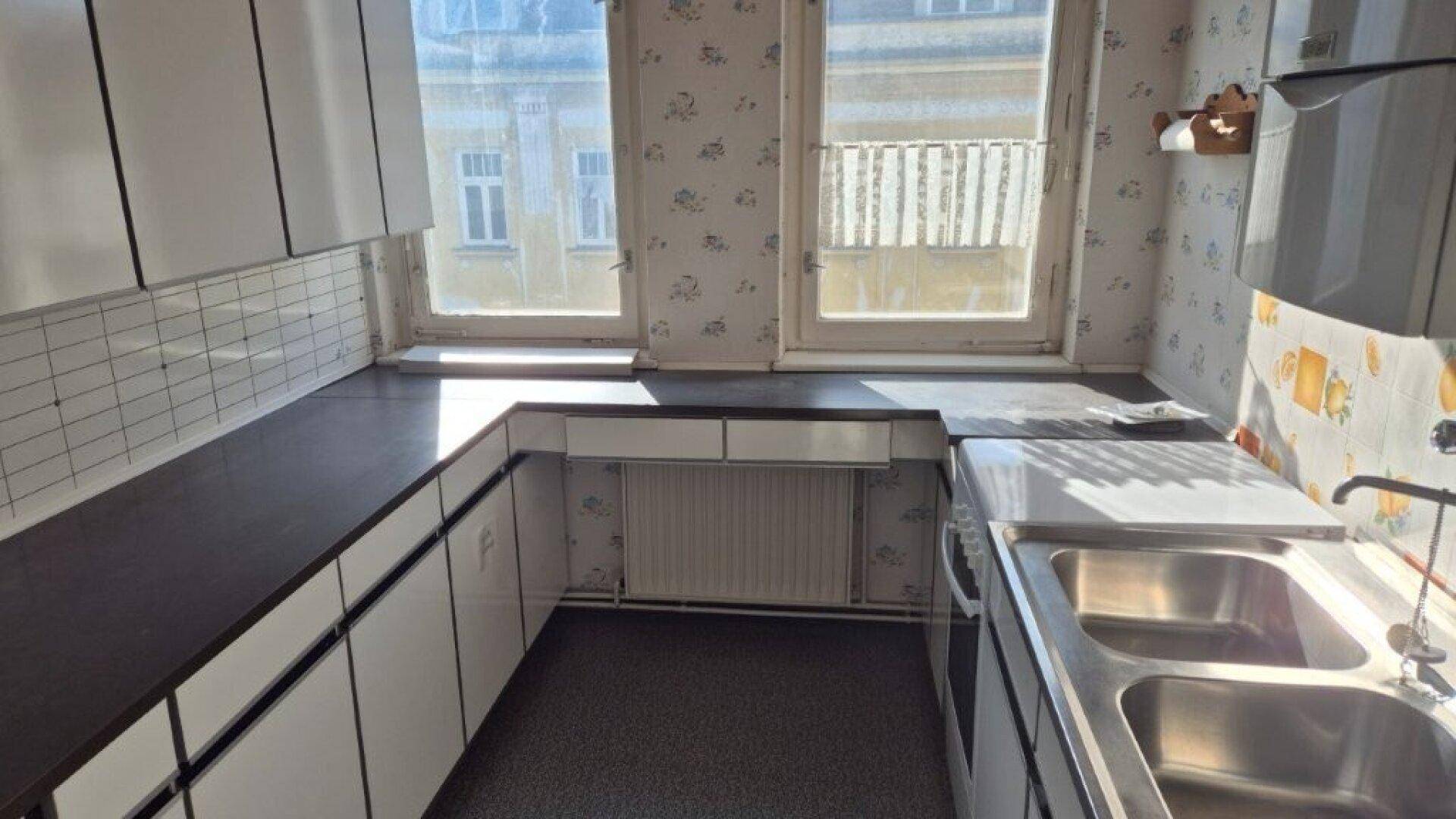 Helle Küche mit weißen Unterschränken, dunkler Arbeitsplatte und Blick nach draußen.