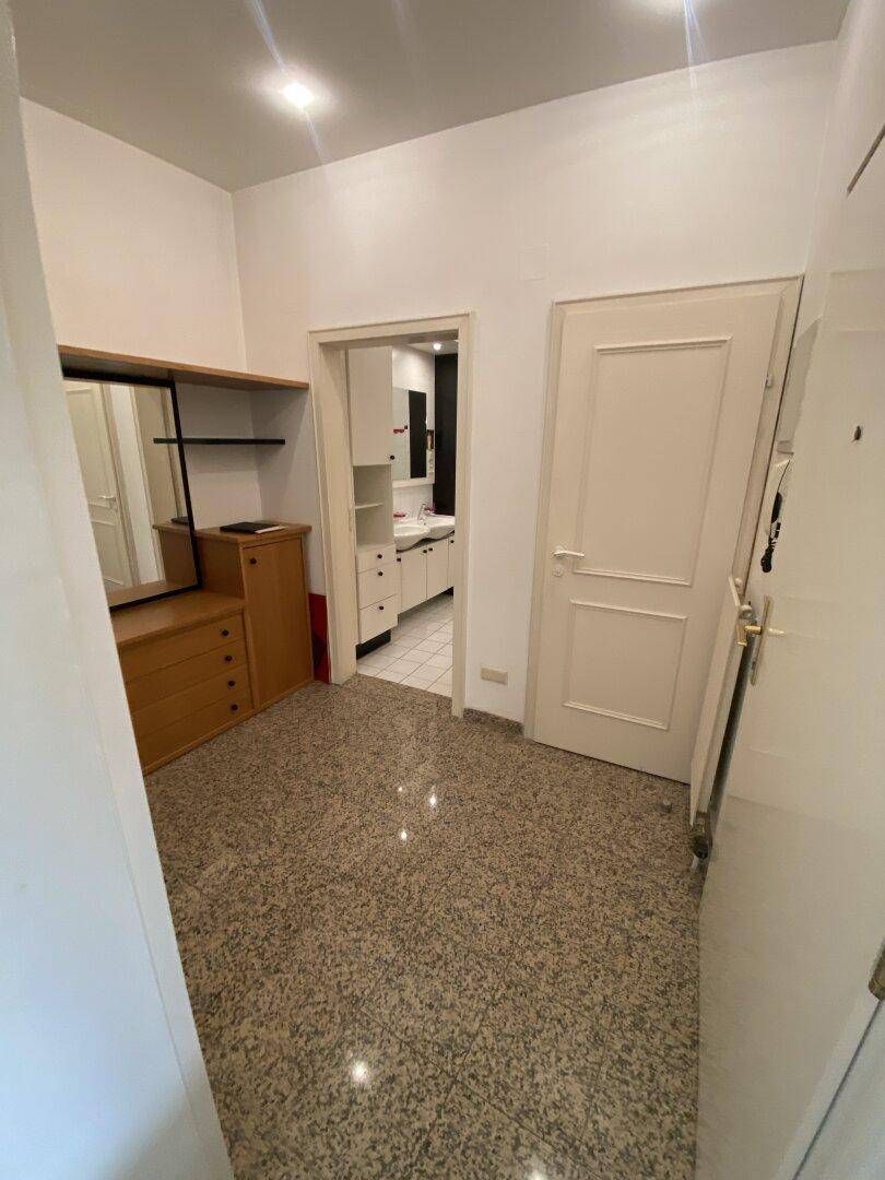 Eingangsbereich mit praktischer Kommode, Spiegel und Blick in das geflieste Badezimmer.
