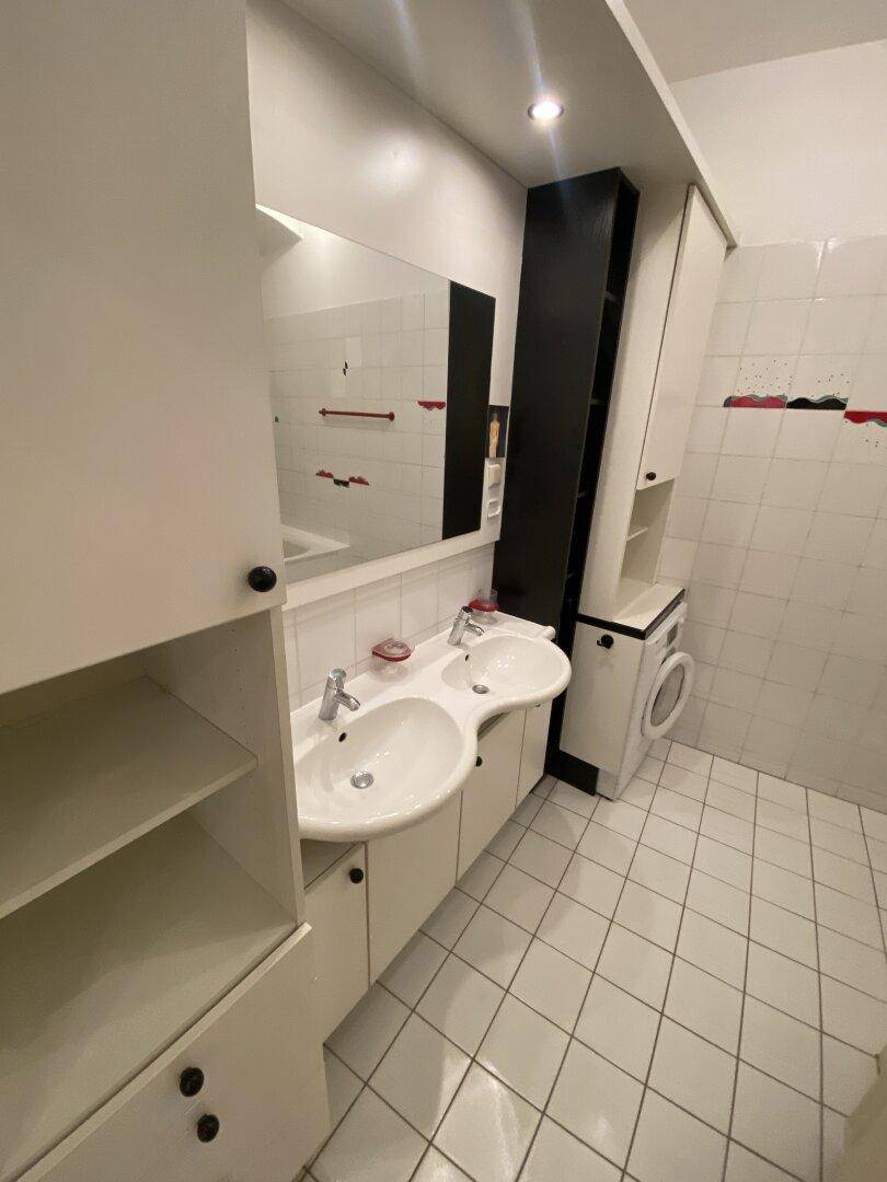 Badezimmer mit Doppelwaschbecken, großem Spiegel, weißen Fliesen und integrierter Waschmaschine.