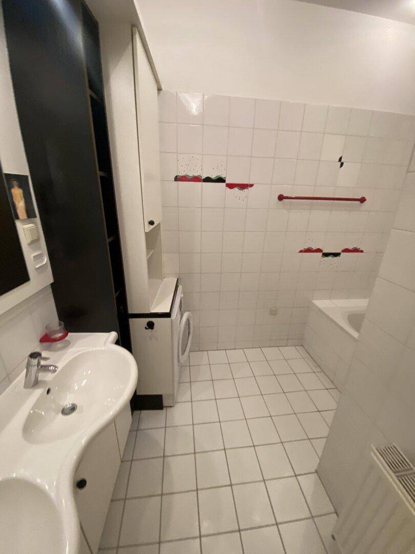 Funktionales Badezimmer mit Doppelwaschbecken, Waschmaschine und weißen Wand- und Bodenfliesen.