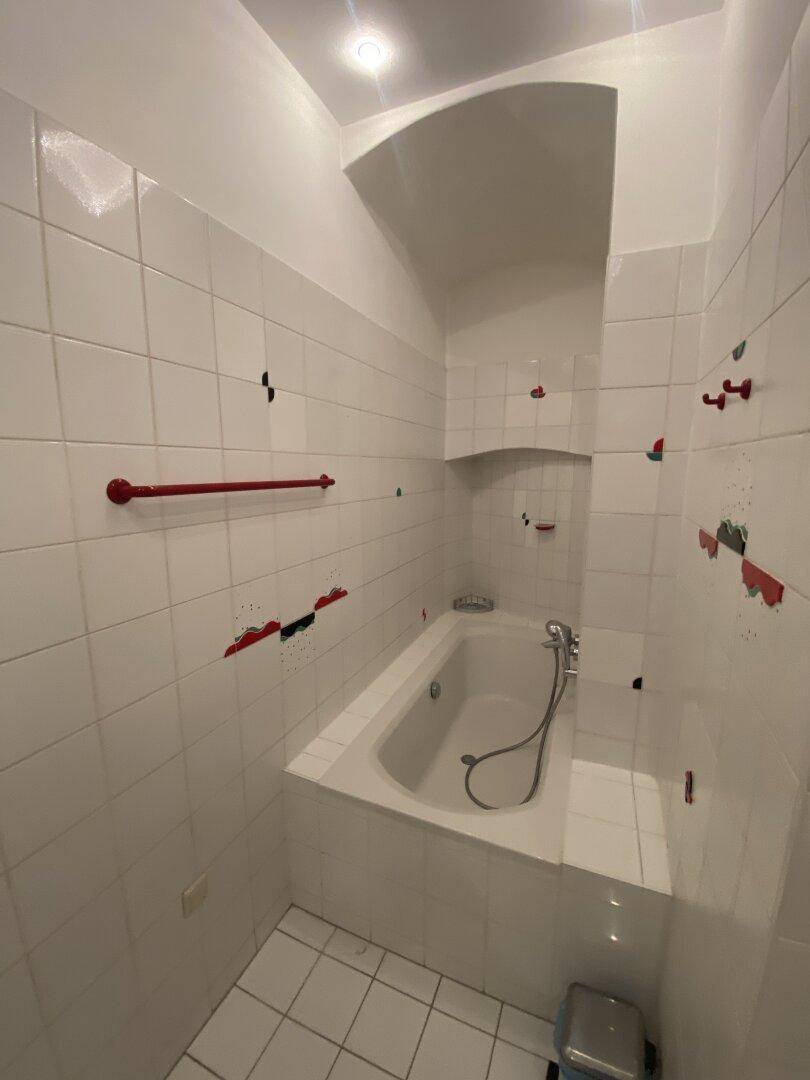 Eingebaute Badewanne in einem gefliesten Badezimmer mit roten Akzenten und praktischer Nische.