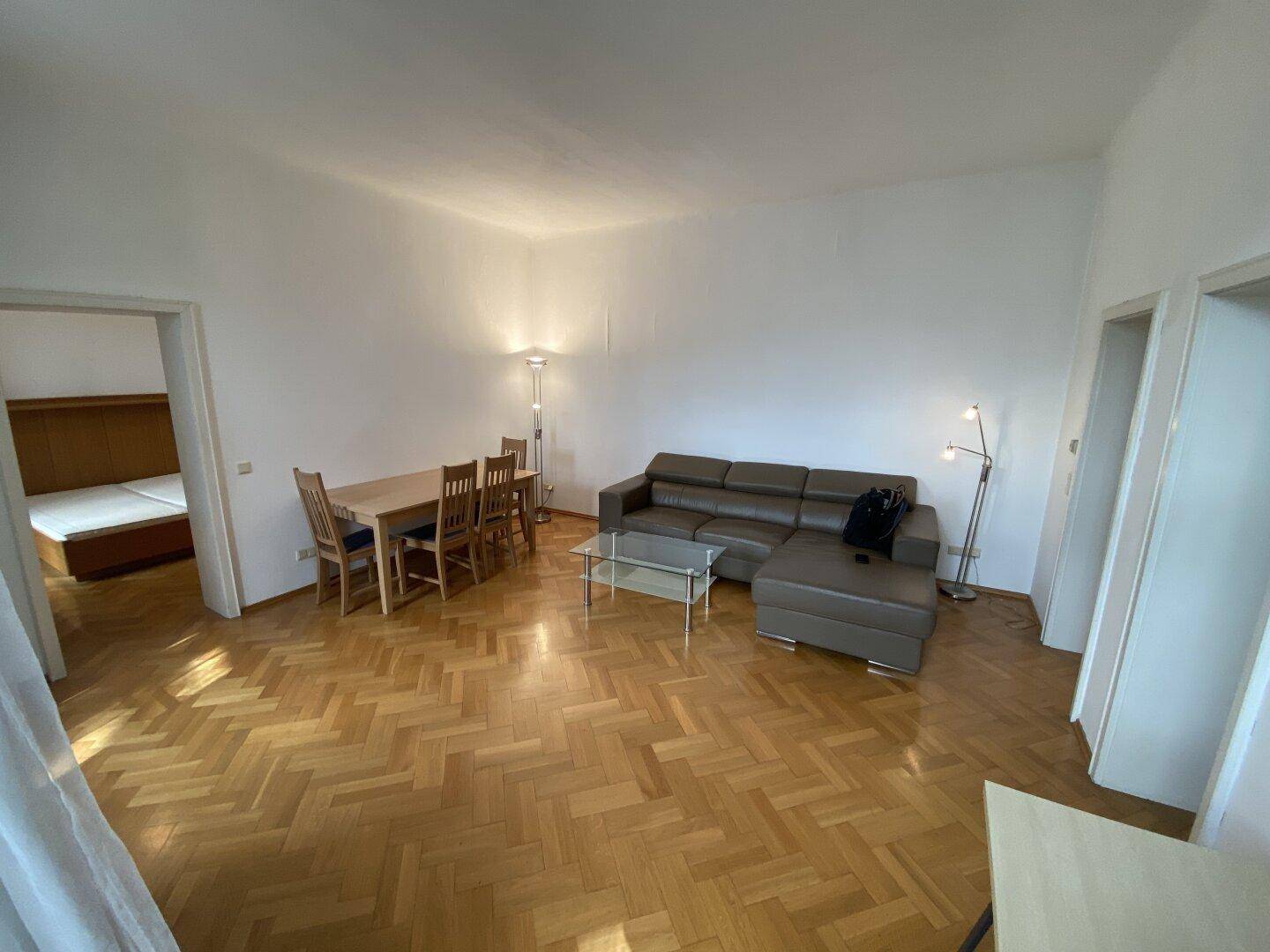 Heller Wohn-Essbereich mit Parkettboden, beigem Ledersofa und Zugang zu einem weiteren Zimmer.