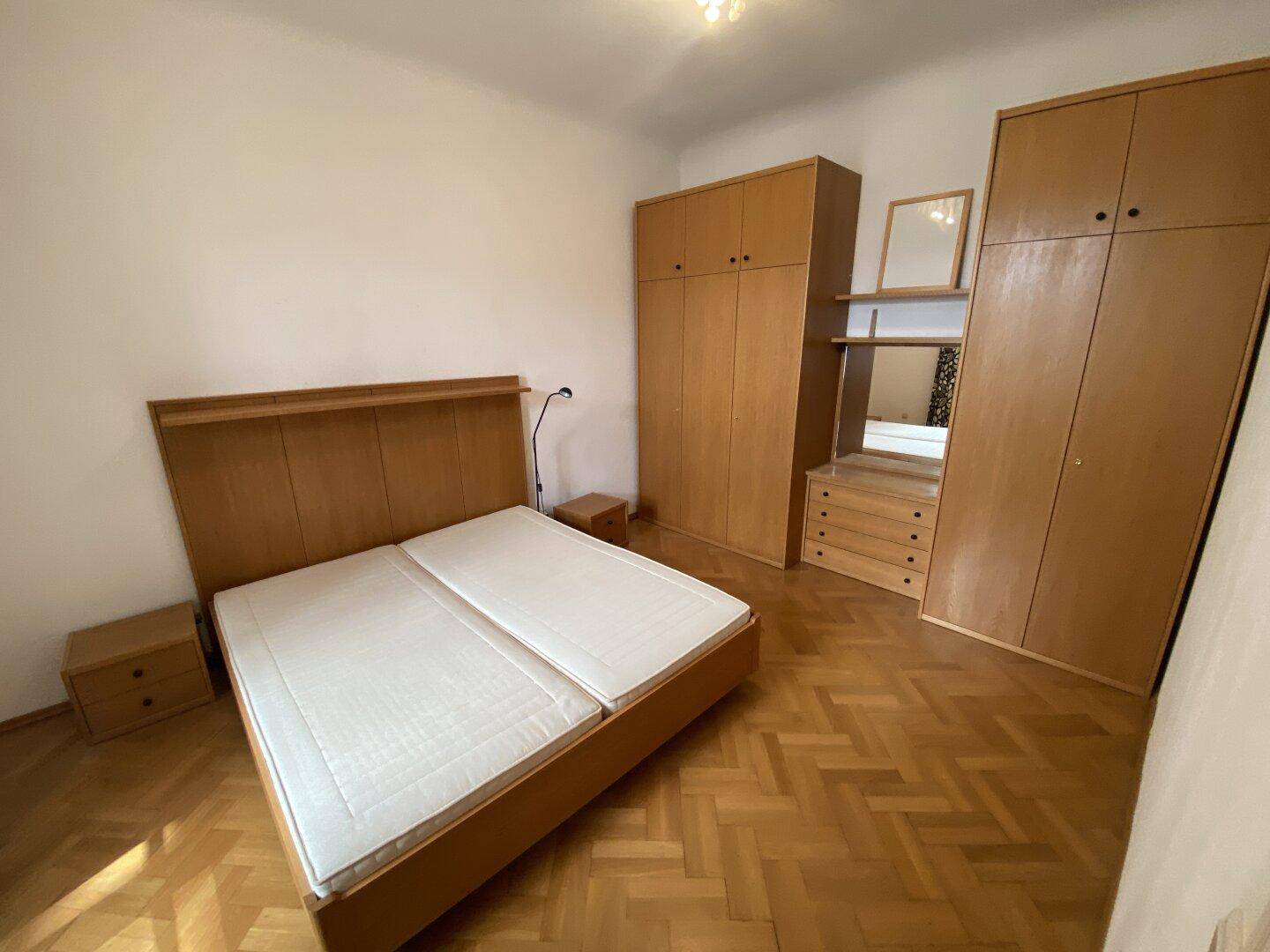 Schlafzimmer mit Doppelbett, Holzschränken und klassischem Fischgrätparkettboden.