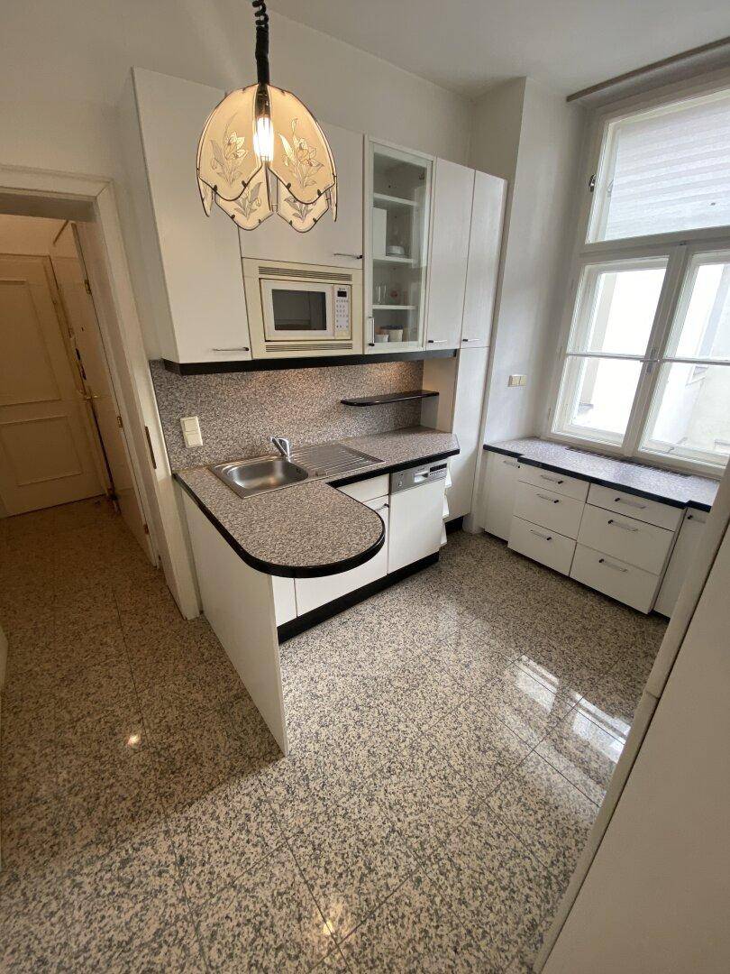 Kompakte Küche mit Einbauschränken, Spüle, Mikrowelle und Fenster, ideal für kleine Haushalte.