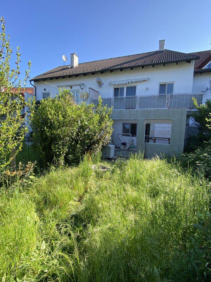 Weitläufiger Gartenbereich hinter dem Haus mit hohem Gras und Büschen.