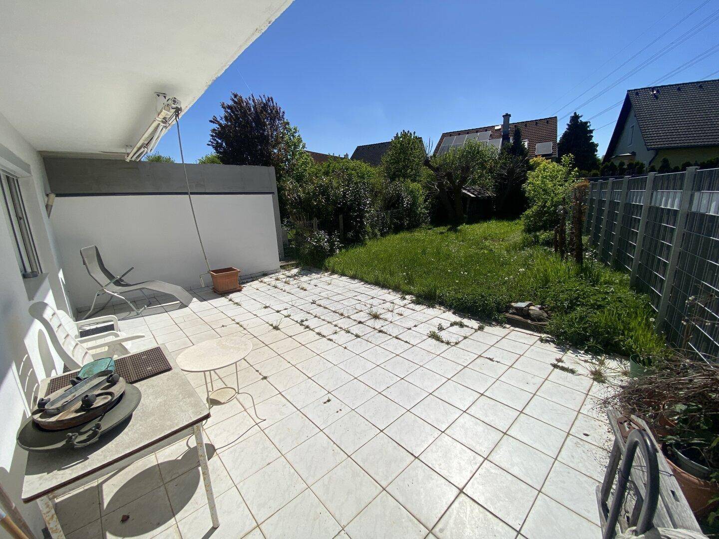 Sonniger Terrassenbereich mit Fliesenboden und Zugang zum Garten.