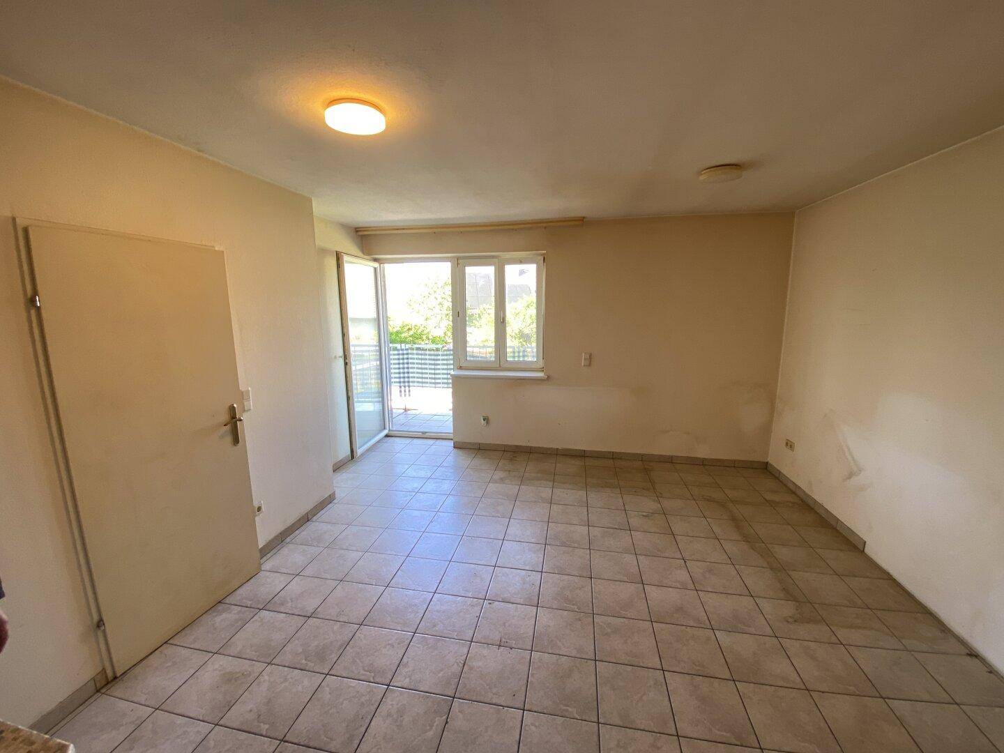 Leeres Wohnzimmer mit Fliesenboden und Zugang zum Balkon.