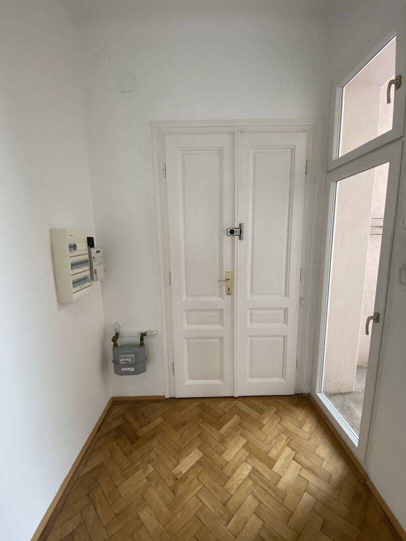 Eingangsbereich mit Fischgrätparkett, Doppeltür und einem Fenster, das zu einem kleinen Balkon führt.