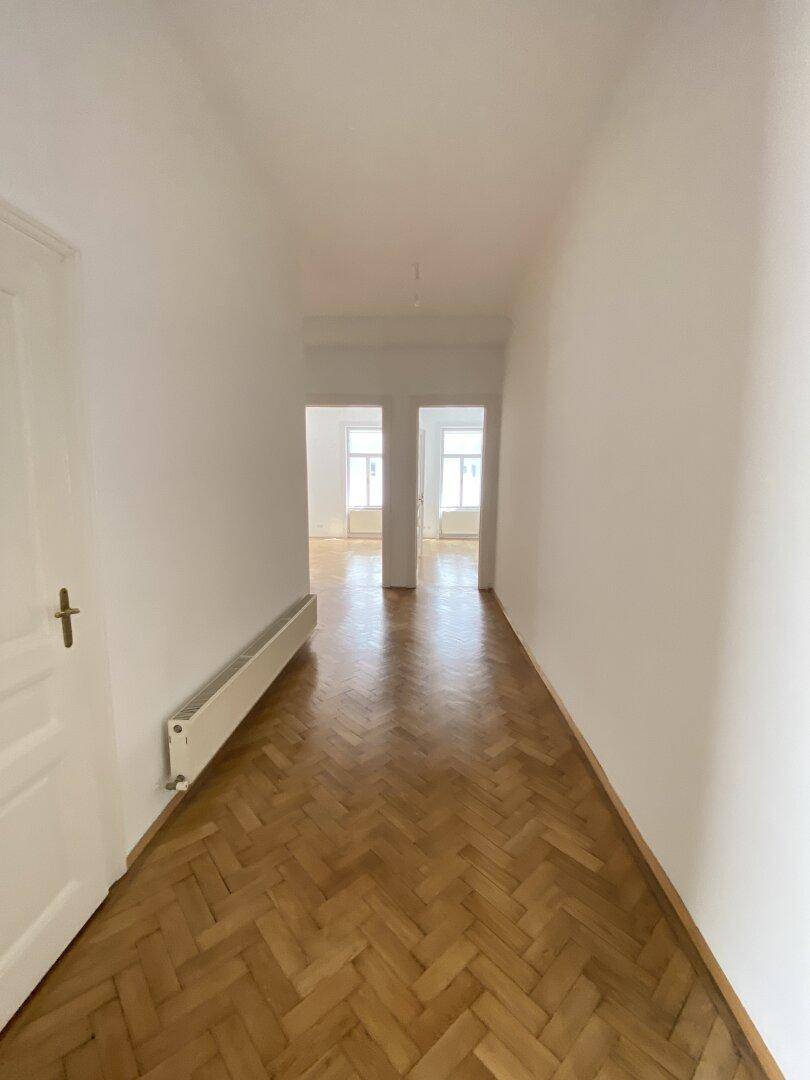 Heller Flur mit Fischgrätparkett, der zu weiteren Räumen mit großen Fenstern führt.