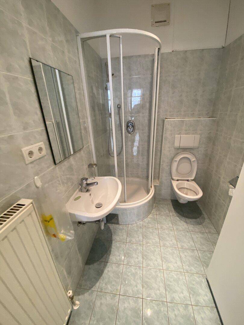 Badezimmer mit Duschkabine, Waschbecken und WC, komplett gefliest in hellem Blau.