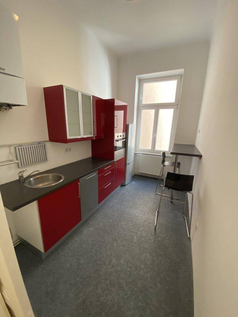 Funktionale Küche mit roten Schränken, Spüle, Kühlschrank und einem Fenster.