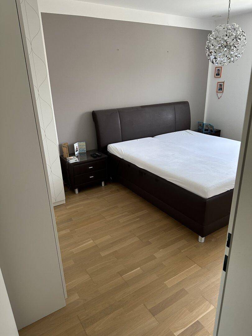 Schlafzimmer mit großem Doppelbett, Nachttischen und hellem Parkettboden, bietet eine ruhige Atmosphäre.