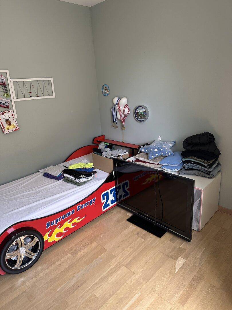 Kinderzimmer mit einzigartigem Autobett und Fernseher, ideal für kleine Rennfahrer.