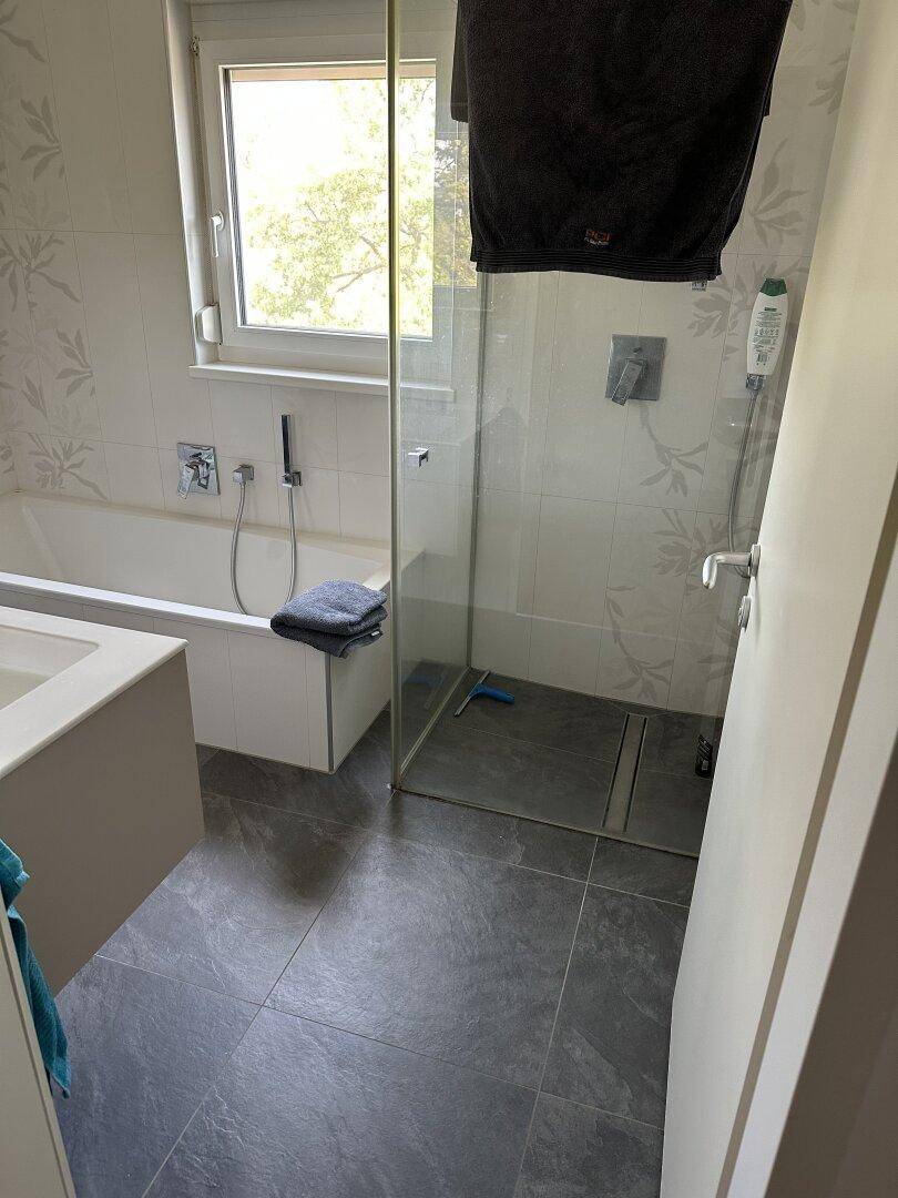 Modernes Badezimmer mit Badewanne, ebenerdiger Dusche und Fenster, ausgestattet mit grauen Fliesen.
