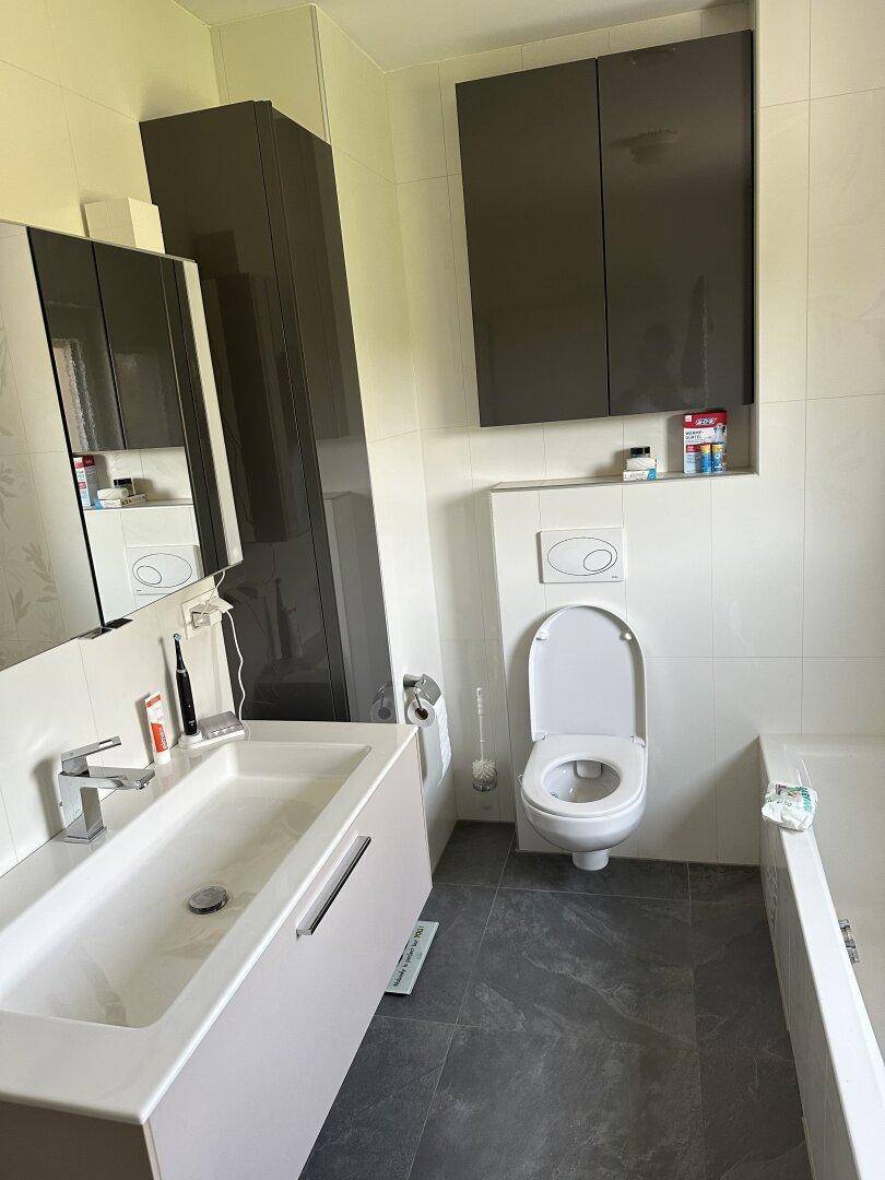 Modernes Badezimmer mit Waschtisch, wandhängendem WC und Badewanne, in hellen Farben gehalten.