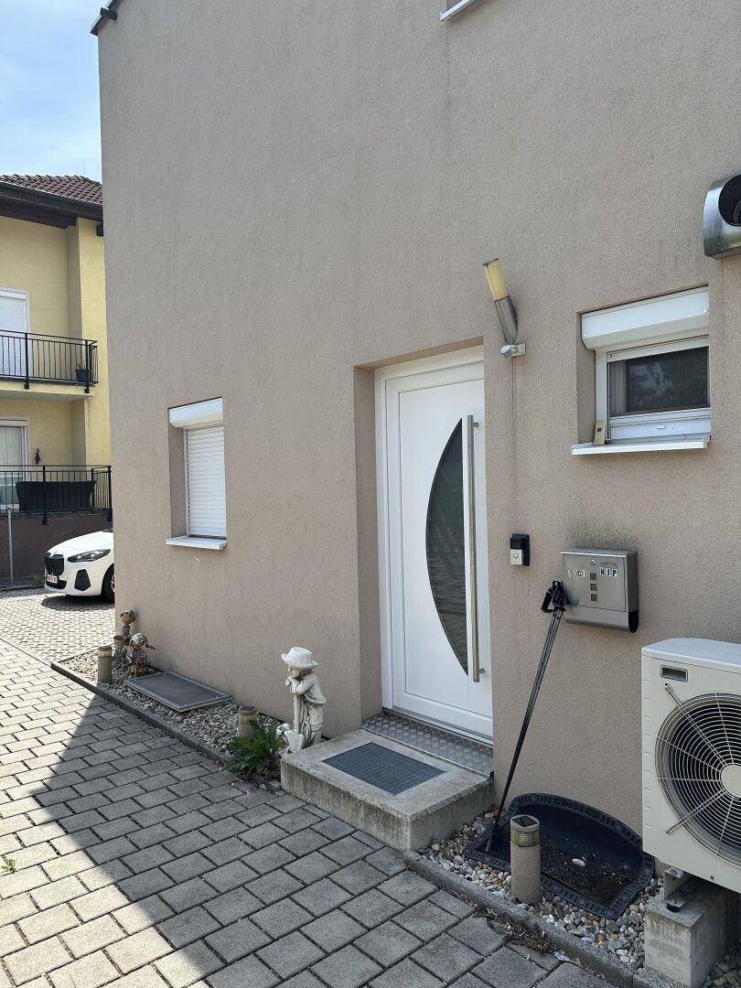 Hauseingang mit moderner Tür und gepflastertem Weg, umgeben von einer gepflegten Außenanlage.