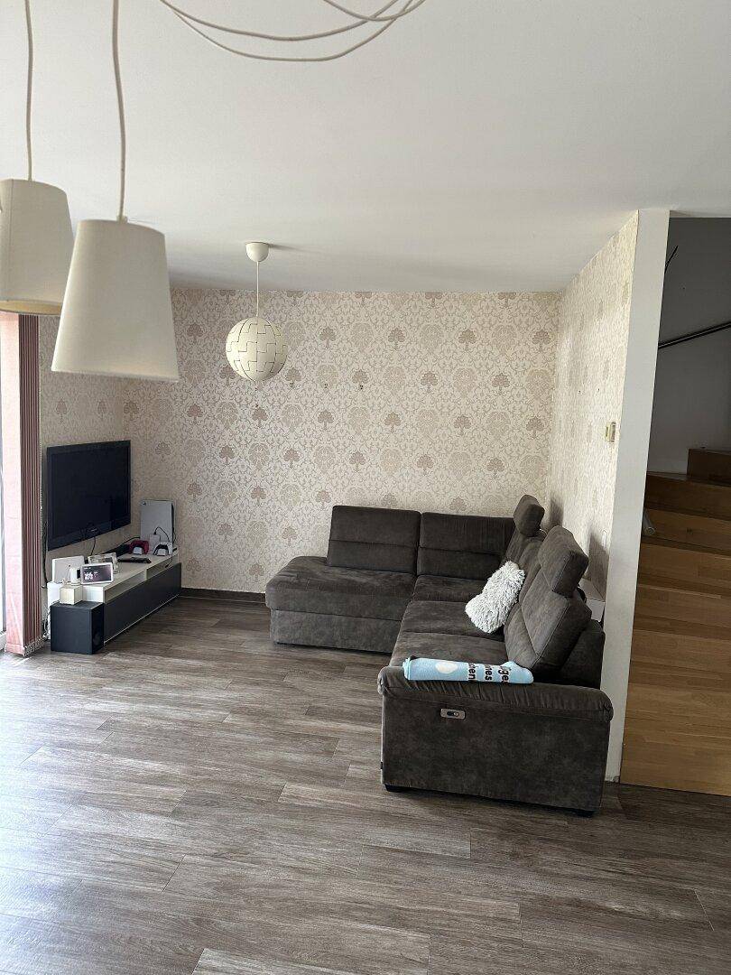 Gemütliches Wohnzimmer mit Ecksofa, Fernseher und dekorativer Tapete, angrenzend an die Treppe.