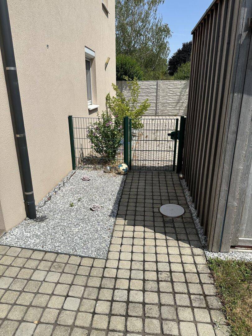 Schmaler Außenbereich mit Kiesweg und gepflastertem Pfad neben dem Haus, mit einem kleinen Gartentor.