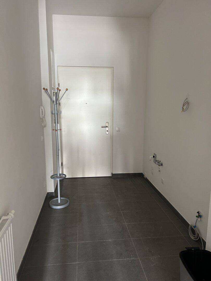 Schlichter Eingangsbereich mit einer Garderobe, Heizkörper und einer einfachen Tür, die zum Raum führt.