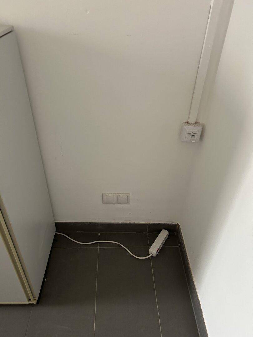 Wandbereich mit Steckdosen und einem Verlängerungskabel auf dem Fliesenboden.