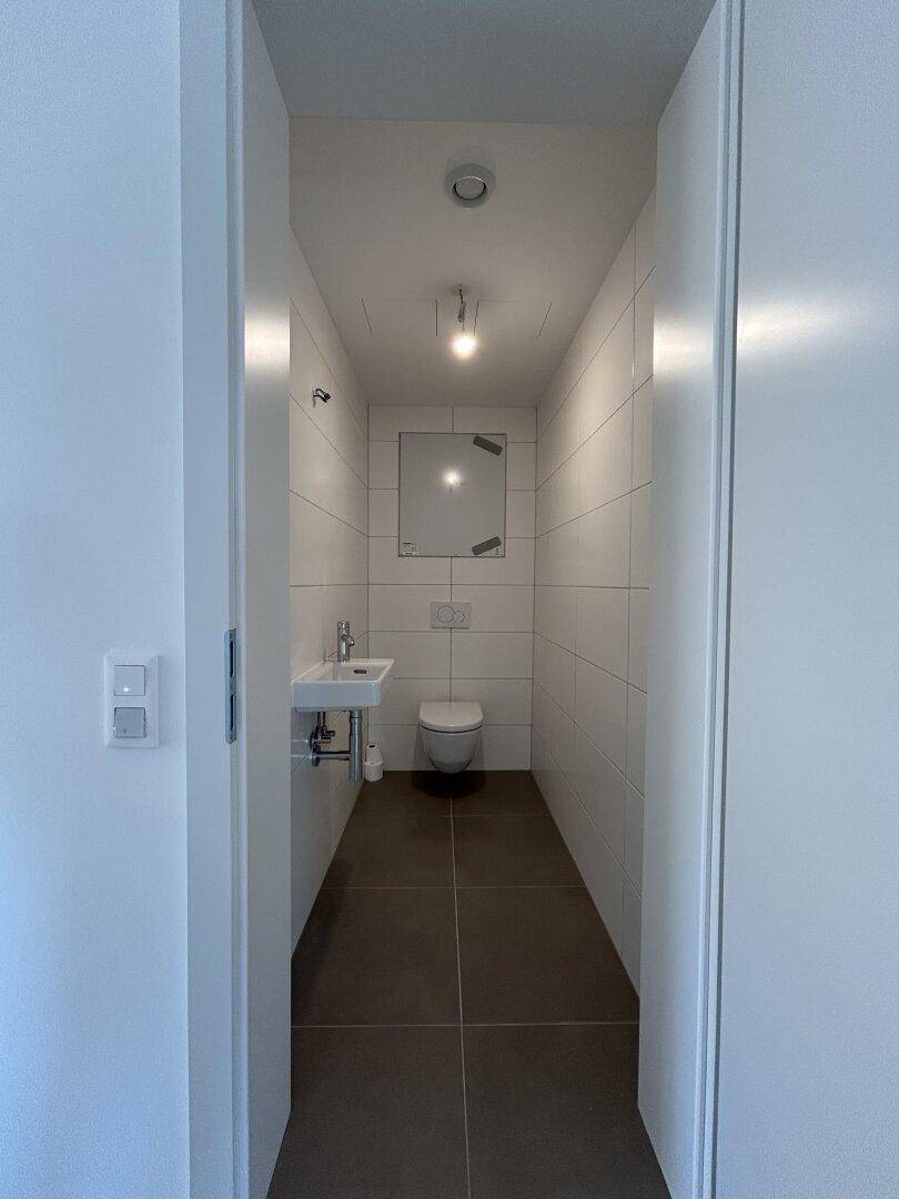 Modernes Gäste-WC mit wandhängendem WC, kleinem Waschbecken und weißen Fliesen.