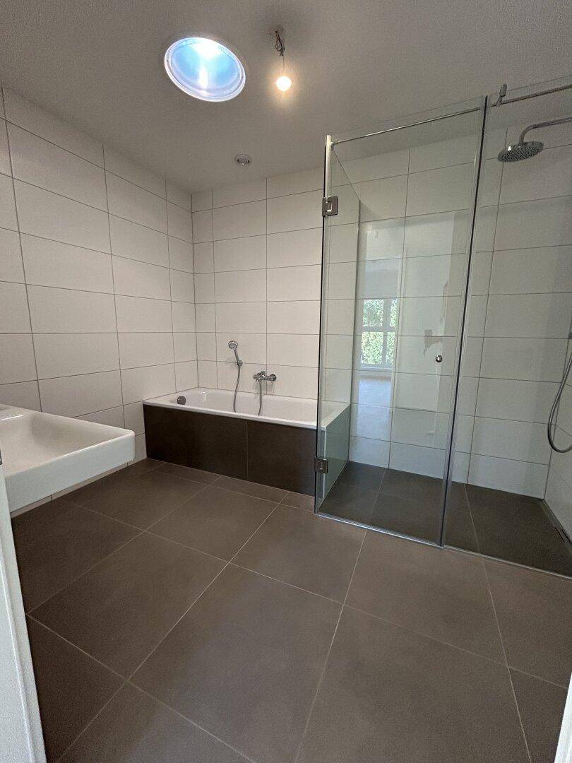 Geräumiges Badezimmer mit Badewanne, ebenerdiger Dusche und dunklen Bodenfliesen.