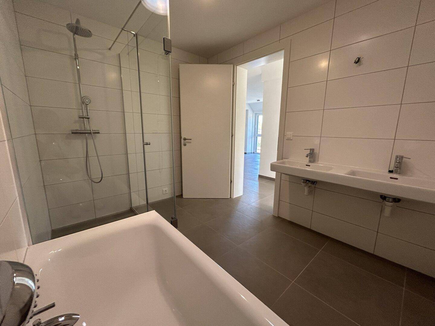 Modernes Badezimmer mit Doppelwaschbecken, Badewanne und großer Glasdusche.