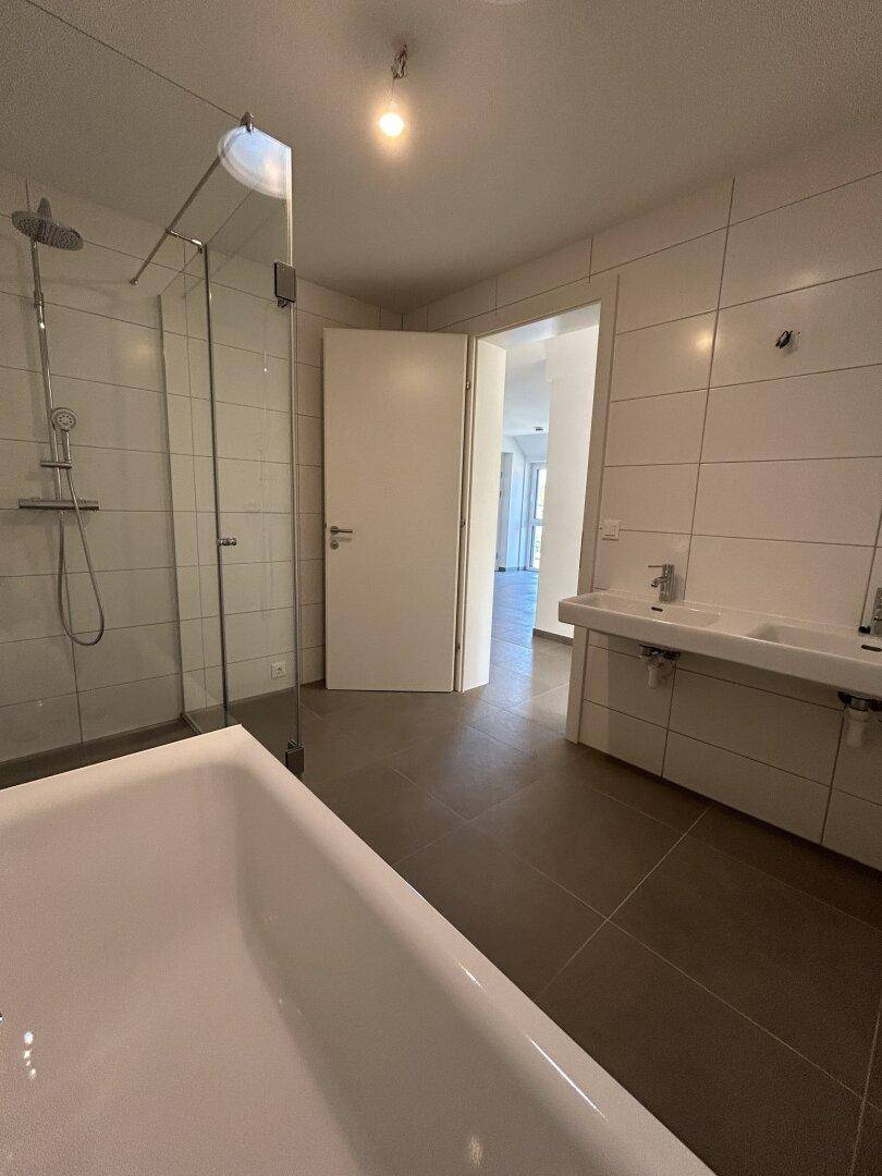 Helles Badezimmer mit Doppelwaschbecken, Badewanne und geräumiger Glasdusche.
