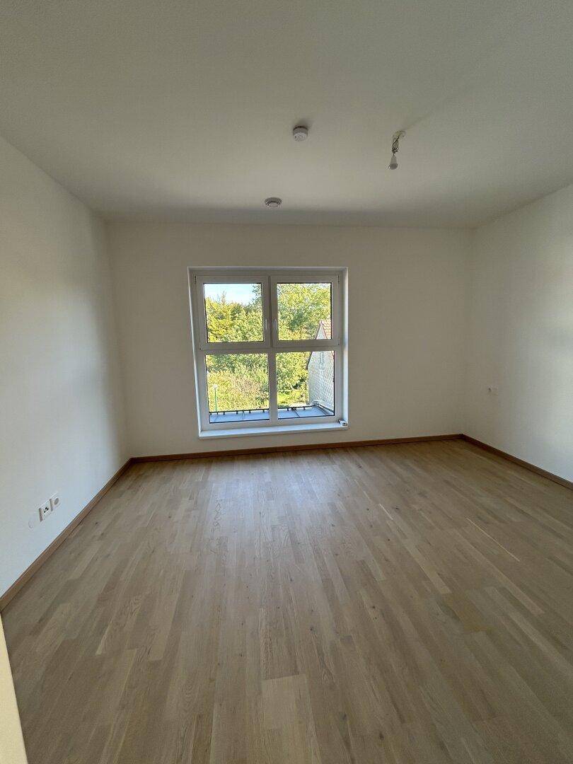 Helles Schlafzimmer mit Holzparkettboden und großem Fenster mit Blick ins Grüne.
