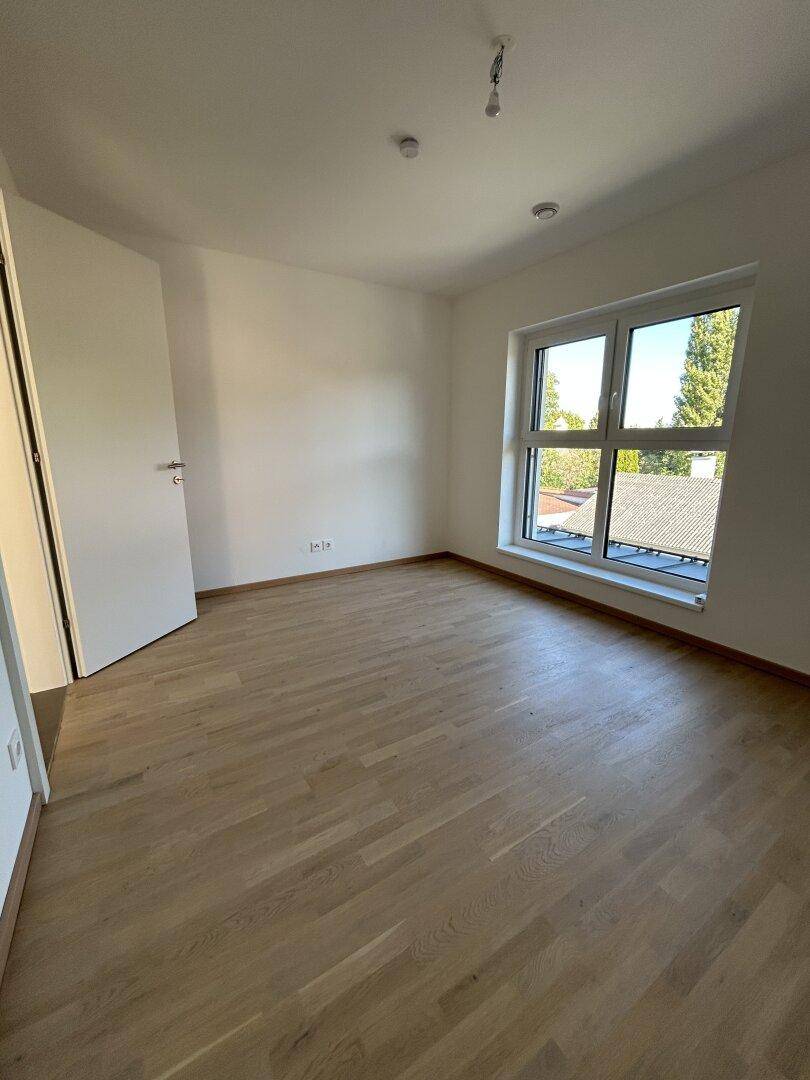 Geräumiges Schlafzimmer mit Holzparkett und viel Tageslicht durch das große Fenster.