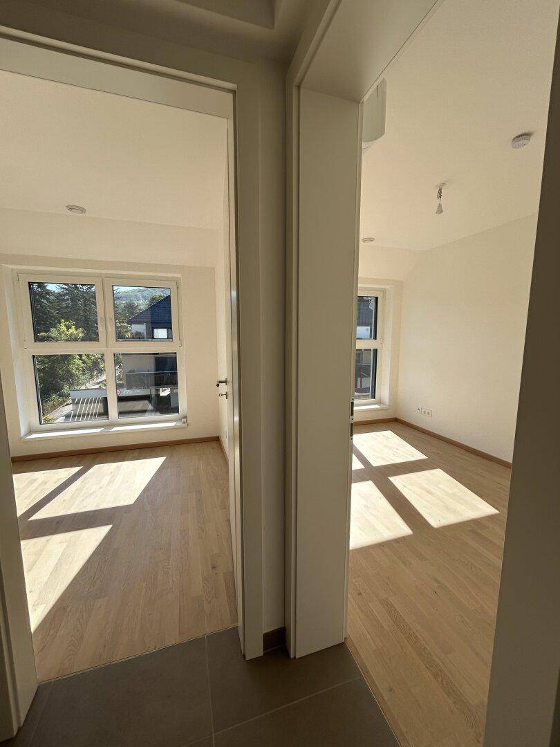 Zwei helle, leere Zimmer mit Holzparkett und Fenstern, die viel Licht hereinlassen.