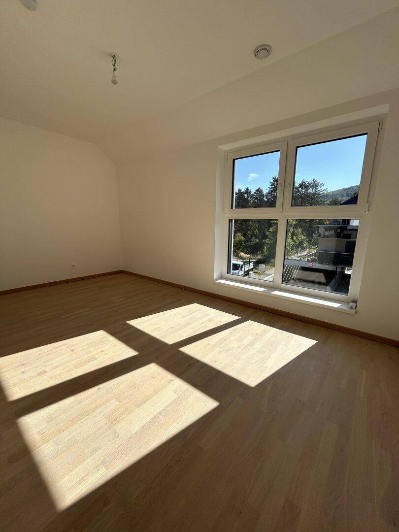 Sonniges Schlafzimmer mit Holzparkettboden und großem Fenster, das viel Licht spendet.