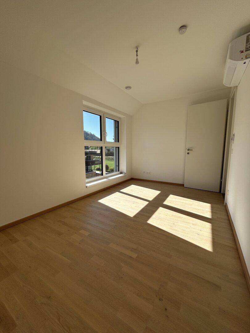 Helles Schlafzimmer mit Holzparkett, Klimaanlage und großem Fenster mit Ausblick.