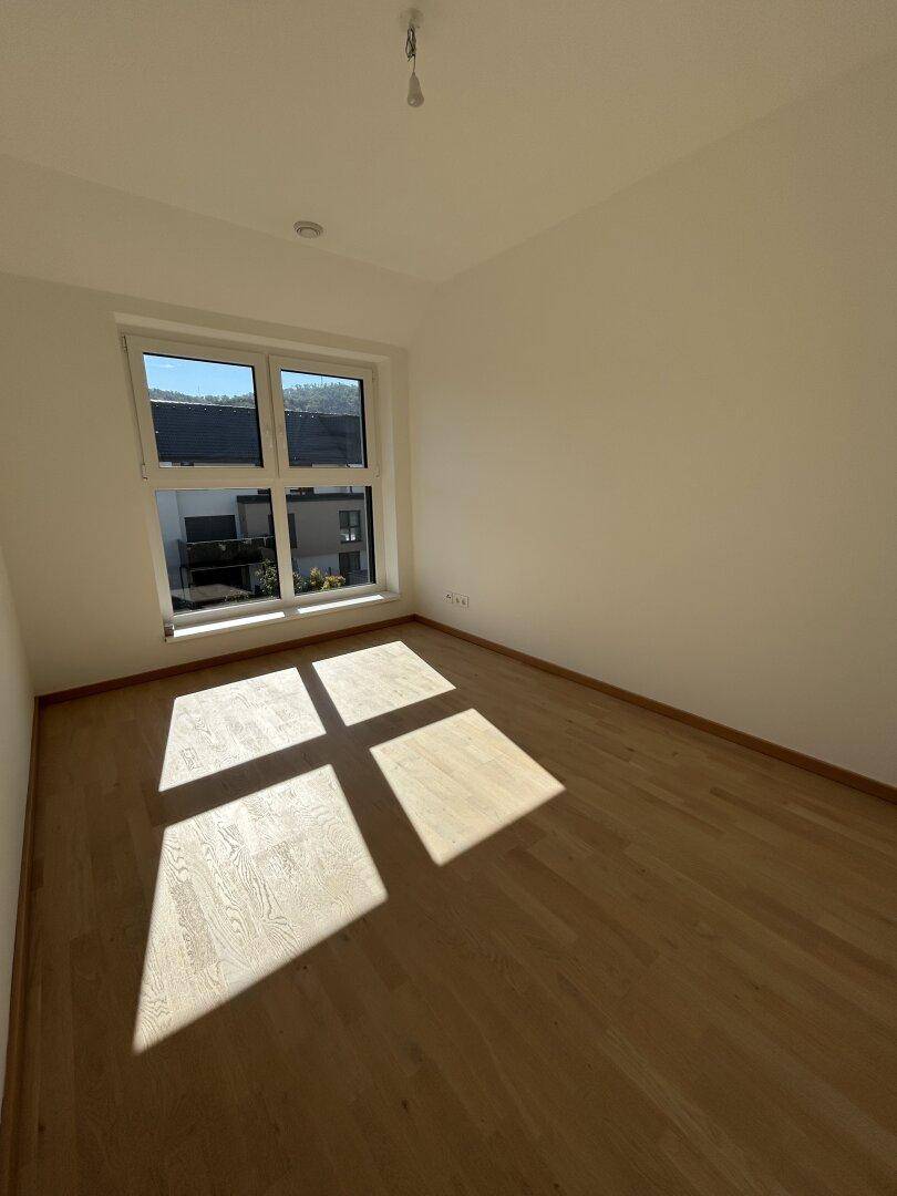 Sonniges Schlafzimmer mit Holzparkettboden und großem Fenster, das den Raum erhellt.