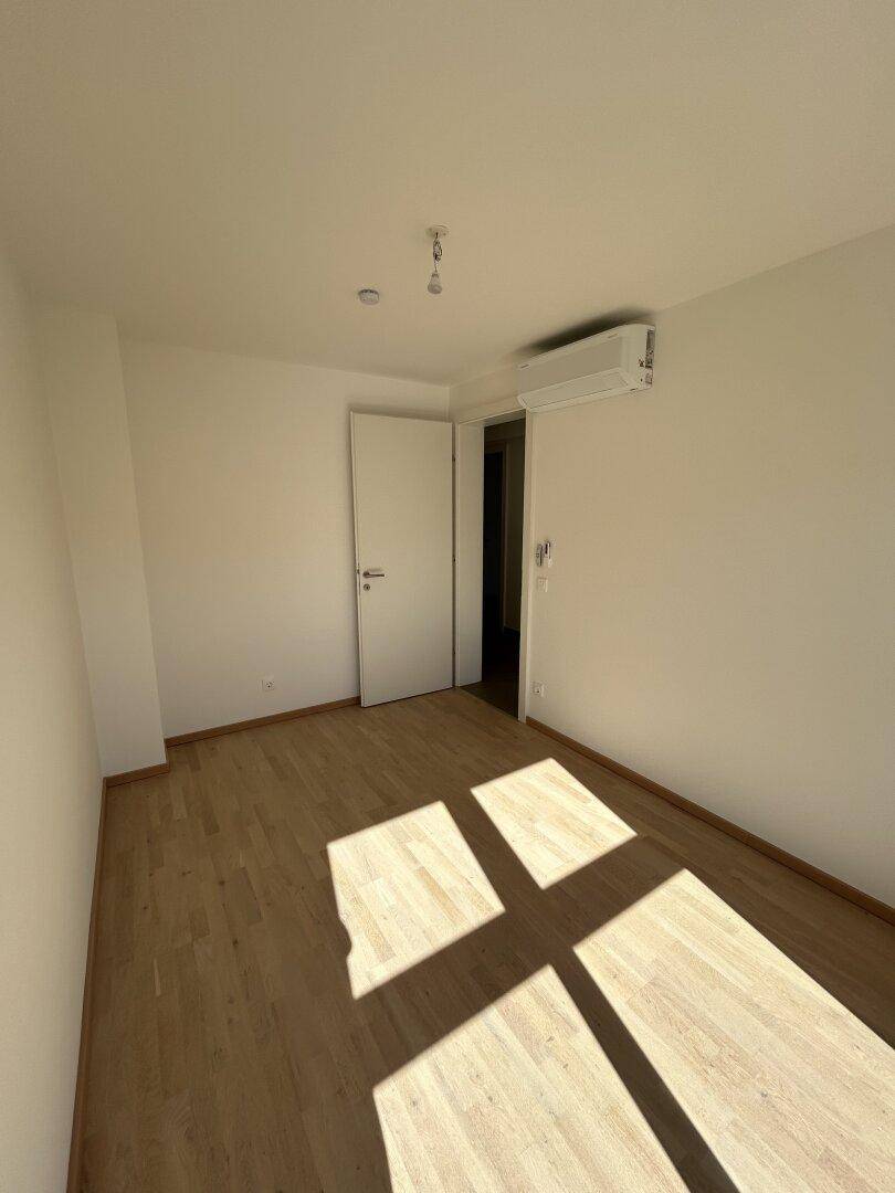 Geräumiges Schlafzimmer mit Holzparkett, Klimaanlage und viel Tageslicht.