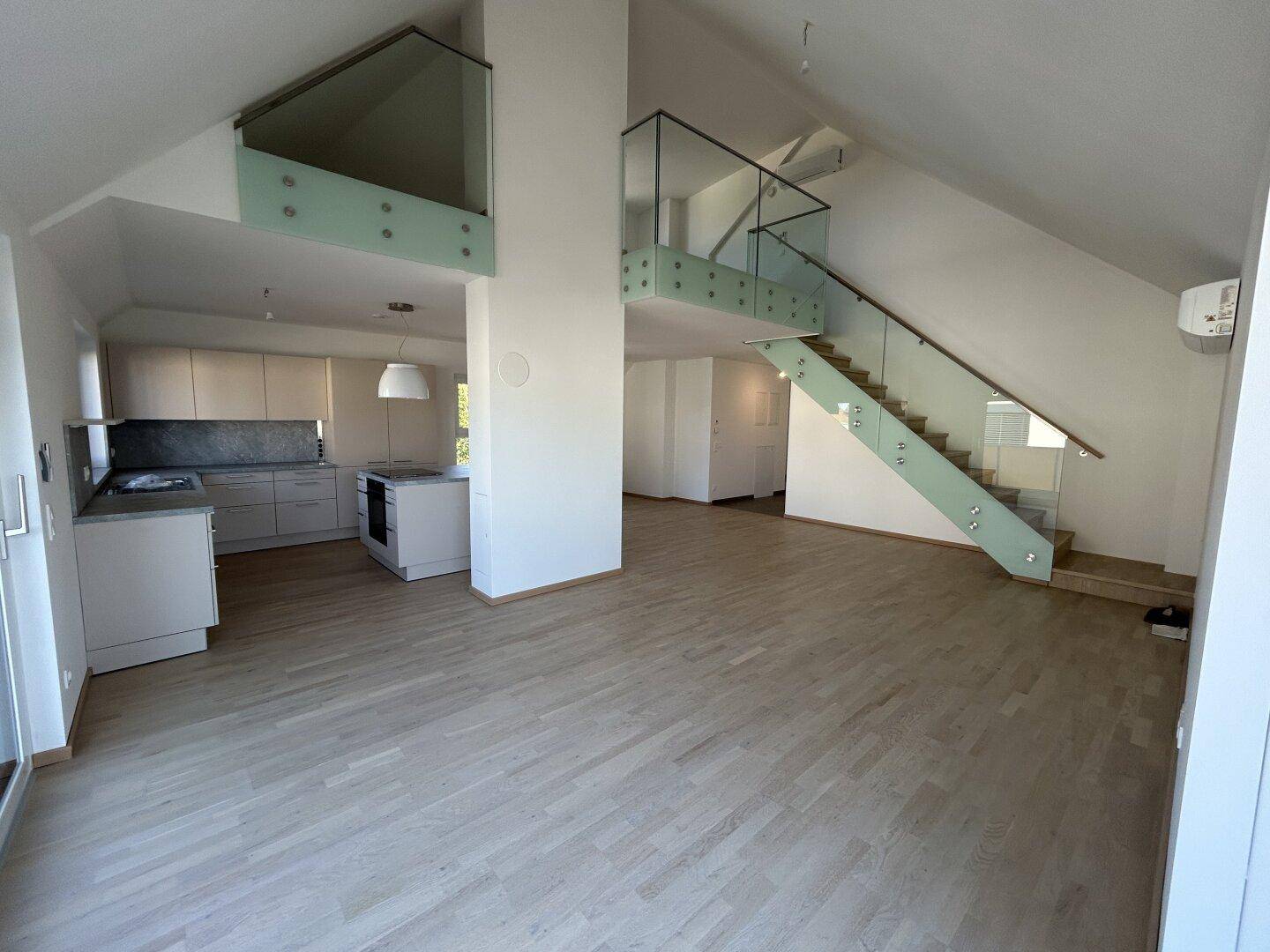 Geräumiger Wohnbereich mit offener Küche, Holzparkett und moderner Glasgeländer-Treppe.